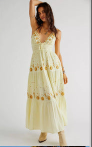 Woman wearing an embroidered cream maxi halter dress with floral patterns on a white background