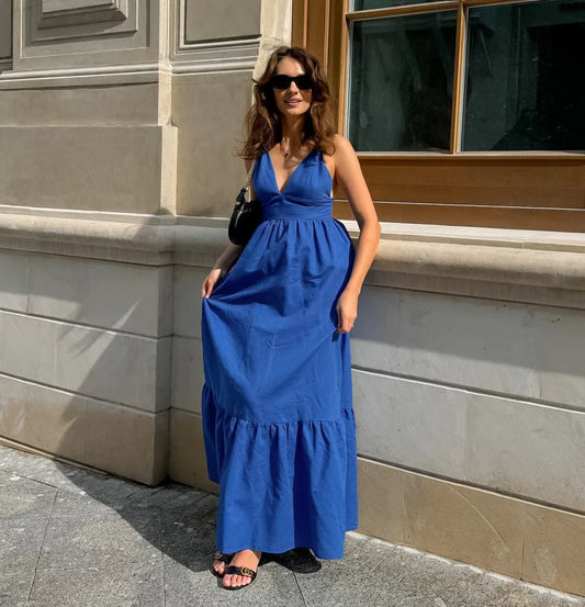 Woman in a blue boho maxi dress standing against a building wall.