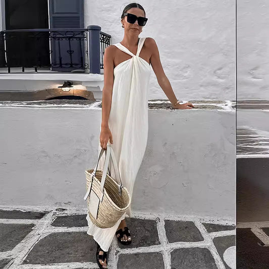 Woman in a white halter style dress standing on a stone pathway with a white wall and black railing in the background.