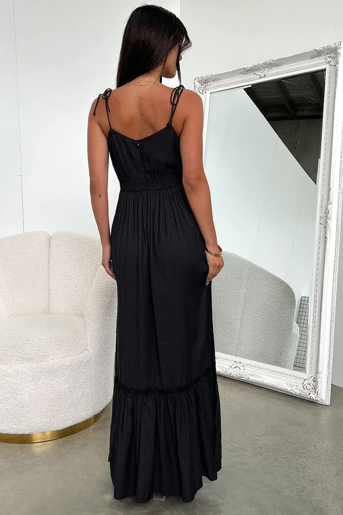 Woman wearing a black maxi boho dress with cut-out design and high slit, standing in a room.