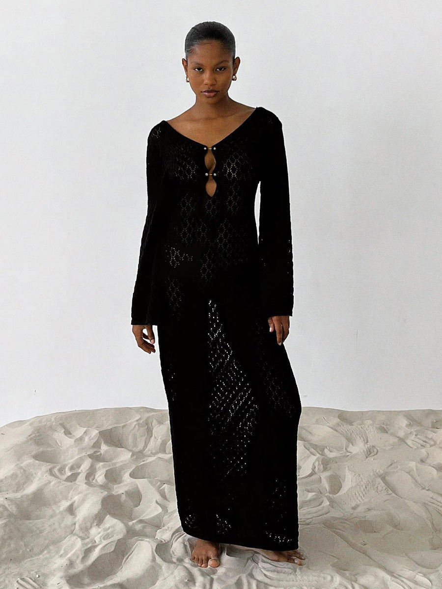 Woman wearing a long black crochet dress with long sleeves standing on sand.
