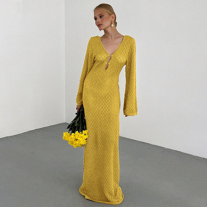 Woman in a long yellow crochet knit dress holding yellow flowers against a white background