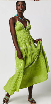 Woman wearing a green floral embroidered maxi halter dress with a white background