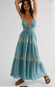 Woman wearing a aqua blue maxi halter dress with floral embroidered patterns on a white background