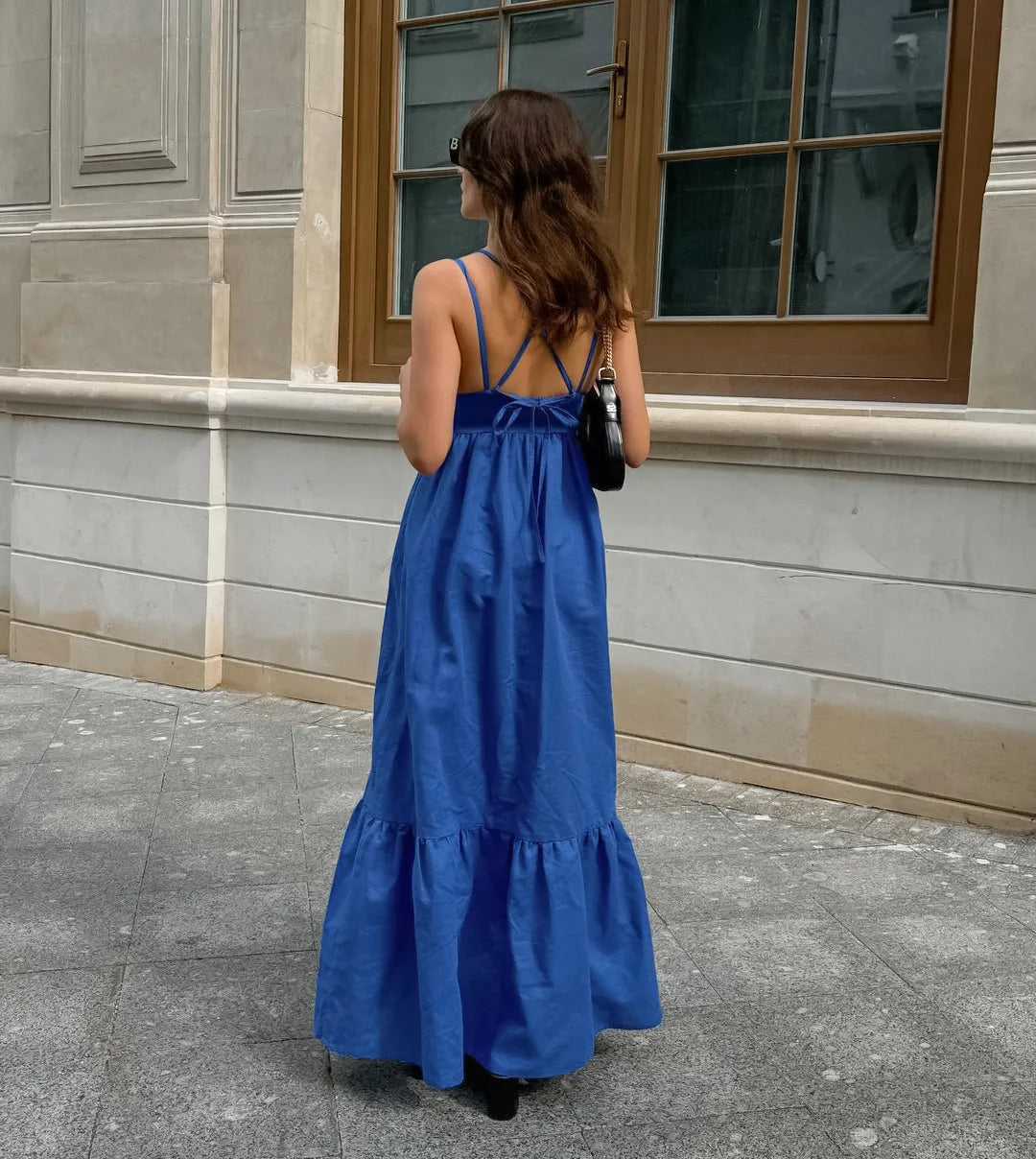 Woman in a blue boho maxi dress standing on a sidewalk next to a building.