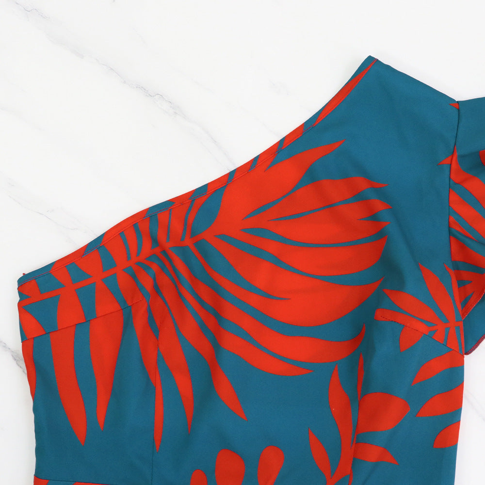 Close up of a teal dress with red tropical leaf pattern on a white background