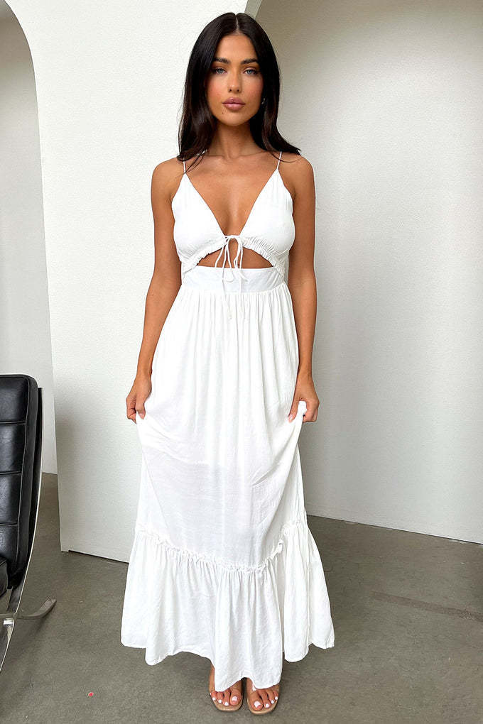 Woman wearing a white maxi boho dress with cut-out design and high slit, standing in a room.