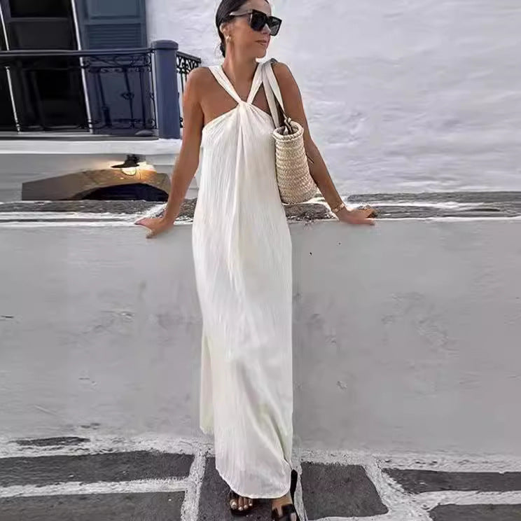 Woman in a white halter style dress standing on a stone pathway with a white wall and black railing in the background.