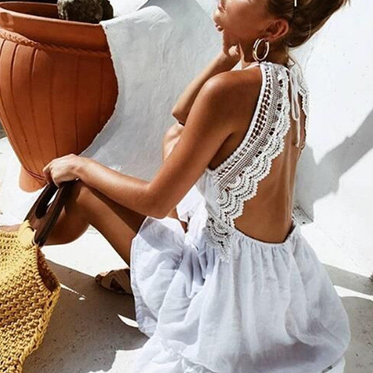 Woman in a short white lace-back dress sitting outdoors.
